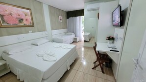 A hotel room with a large bed, a smaller bed, a desk with a chair, a TV, and a painting of flowers on the wall. - Pousada Caroline (Foz do Iguaçu)