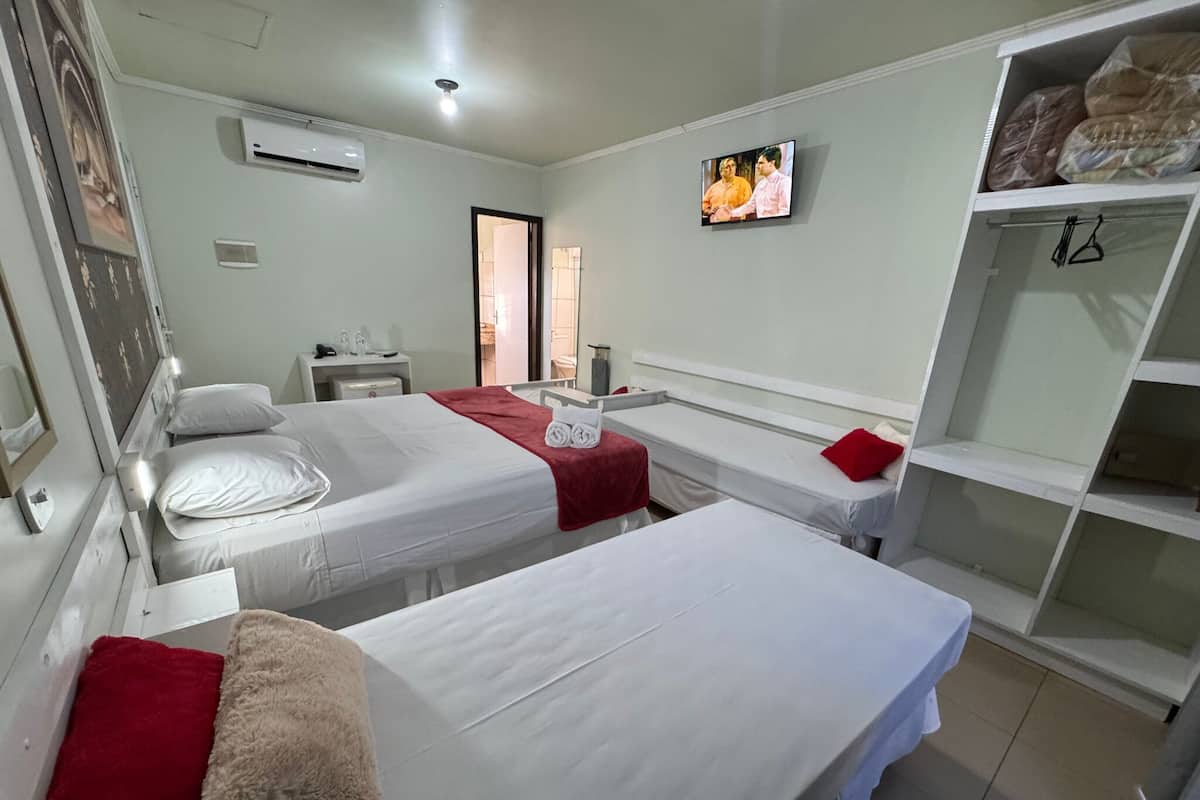 A hotel room with two single beds, a TV, a wardrobe, and a bathroom visible through an open door.