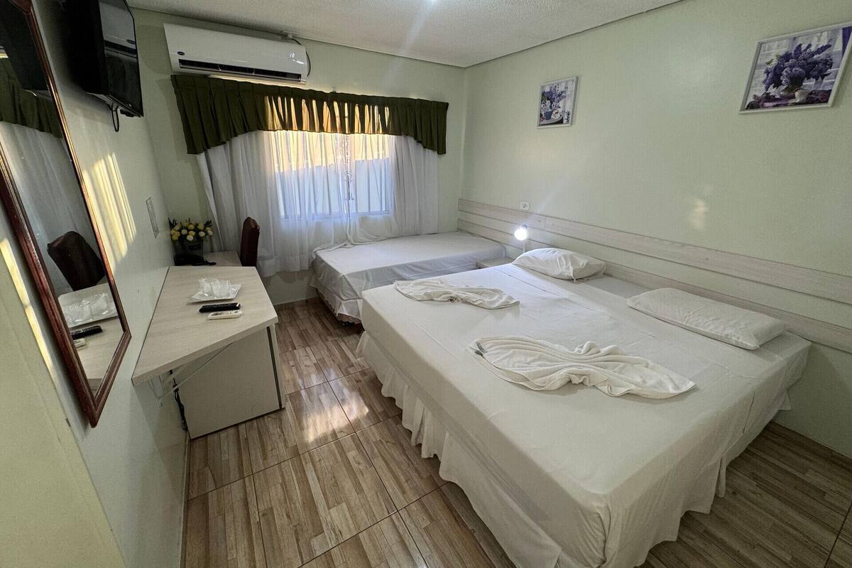 A hotel room with a bed, bedside table, mirror, and an air conditioning unit.