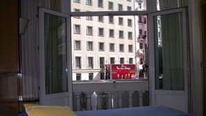 A hotel room with a bed, a window with a view of a building, and a red sign on the window sill. - Hostal Buenos Aires (Madrid)