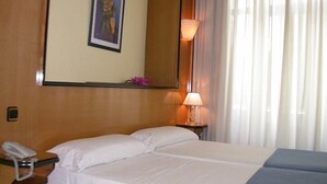 A hotel room with a bed, a bedside table with a lamp, a phone, and a painting on the wall. - Hostal Buenos Aires (Madrid)