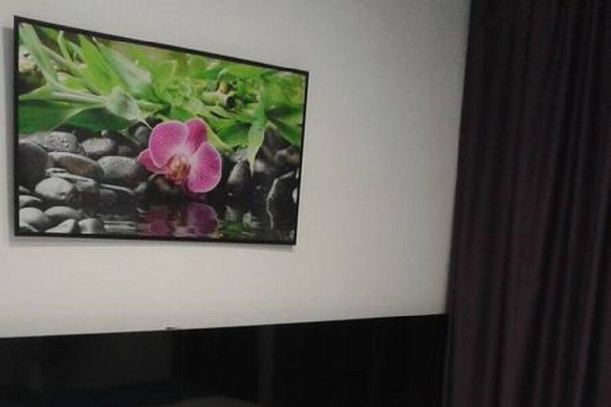 A room with four beds, each with a white mattress and a blue blanket. There is a painting of a pink orchid on the wall above the beds.