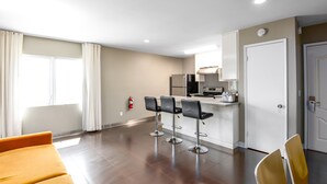 A modern kitchen with a refrigerator, microwave, and stove. There are three black bar stools and a yellow chair. A fire extinguisher is mounted on the wall.