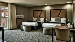 A hotel room with two beds, a desk, a chair, and a view of the outside.