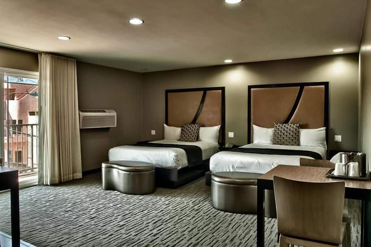 A hotel room with two beds, a desk, a chair, and a view of the outside.