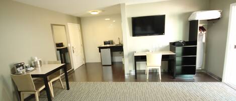 Habitación de hotel con comedor, kitchenette, televisión de pantalla plana montada en la pared y una pequeña zona de estar con sofá.