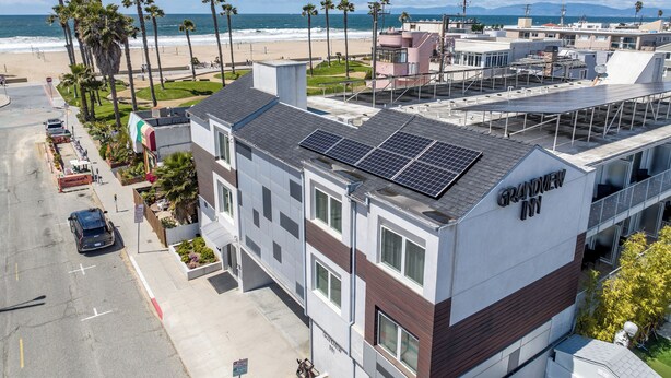 A hotel with a rooftop solar panel installation, located near a beach with palm trees and a clear sky.