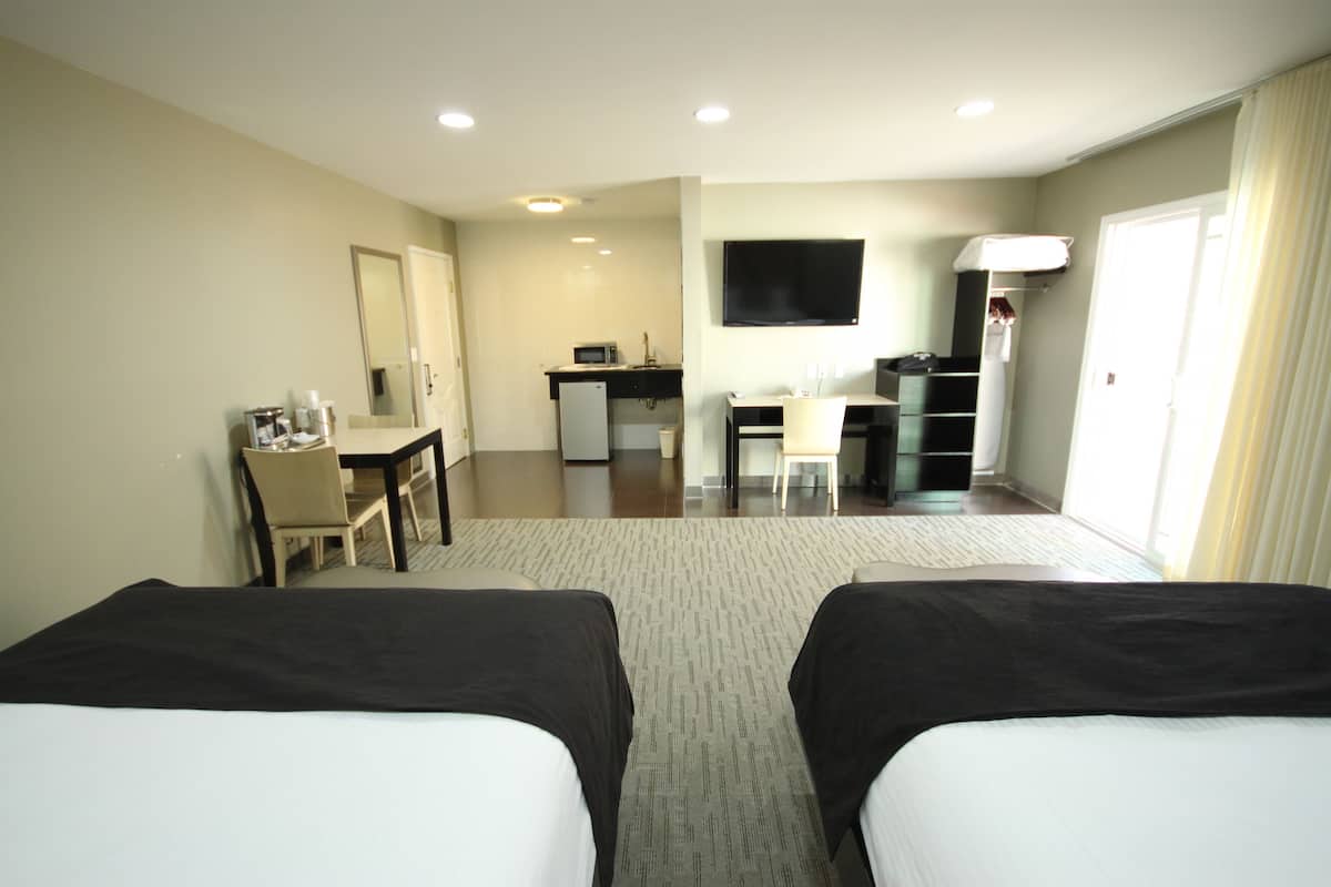 A hotel room with two beds, a desk, a chair, a TV, and a kitchenette.