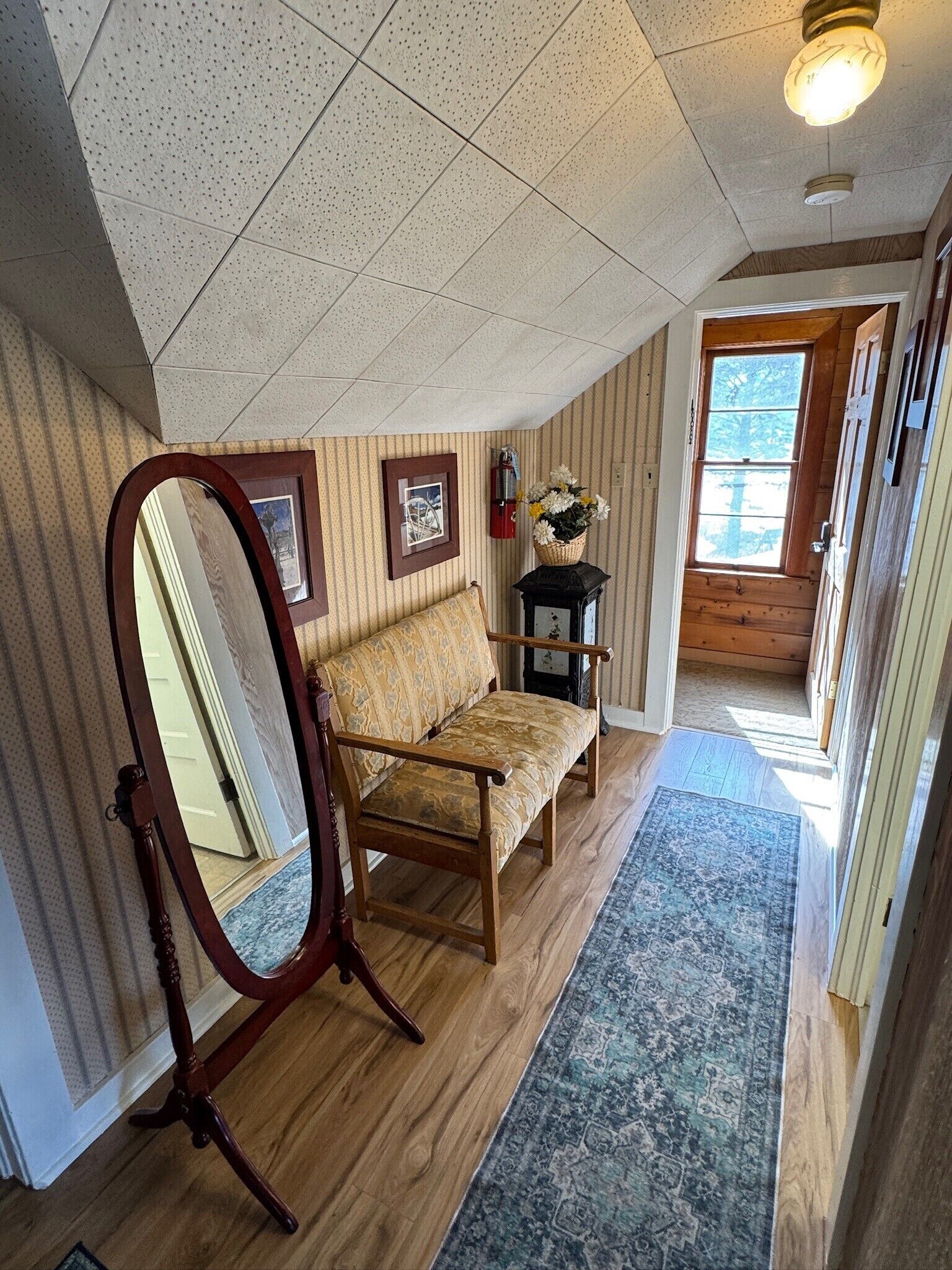 A room with a wooden floor, a sofa, a mirror, a rug, and a window with a view of trees.