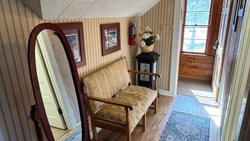 Une pièce avec un plancher en bois, un canapé, un miroir, un tapis et une fenêtre donnant sur des arbres.