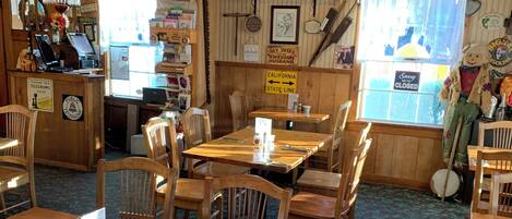 A restaurant interior with wooden tables and chairs, a counter with a telephone, and various signs and decorations on the walls.
