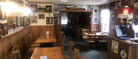 Un restaurante con mesas y sillas de madera, cuadros en las paredes y un letrero para un teléfono público.