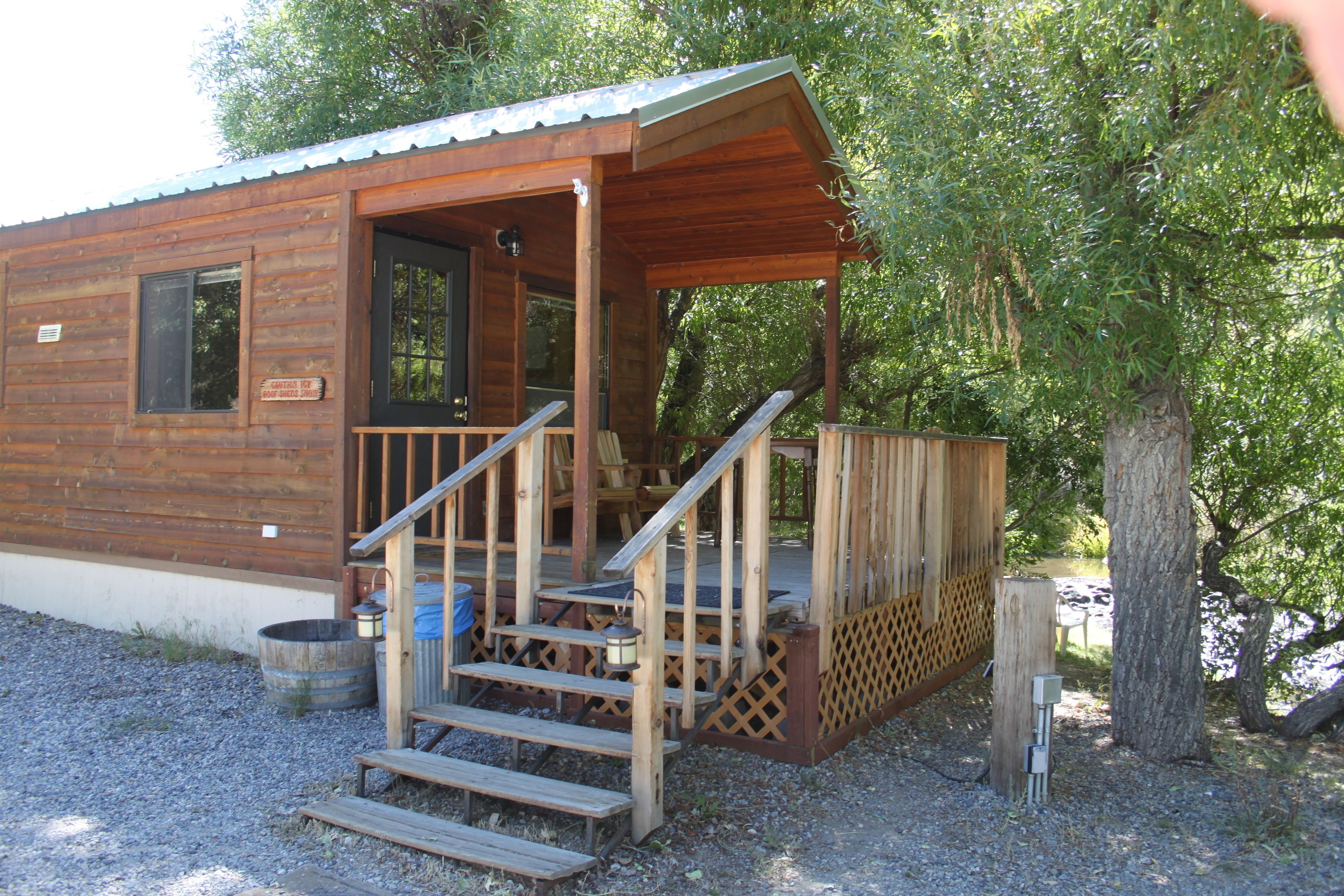 Eine Holzhütte mit Veranda, Treppe und einer kleinen Sitzgelegenheit im Freien.