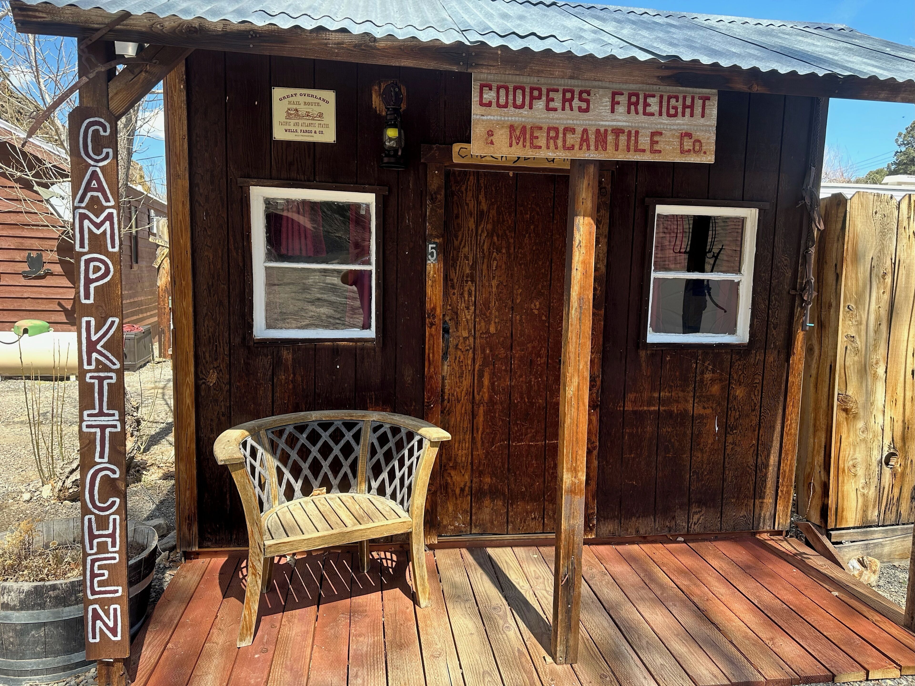 A rustic wooden cabin with a sign reading "COOPERS FREIGHT & MERCANTILE CO." and a bench in front.