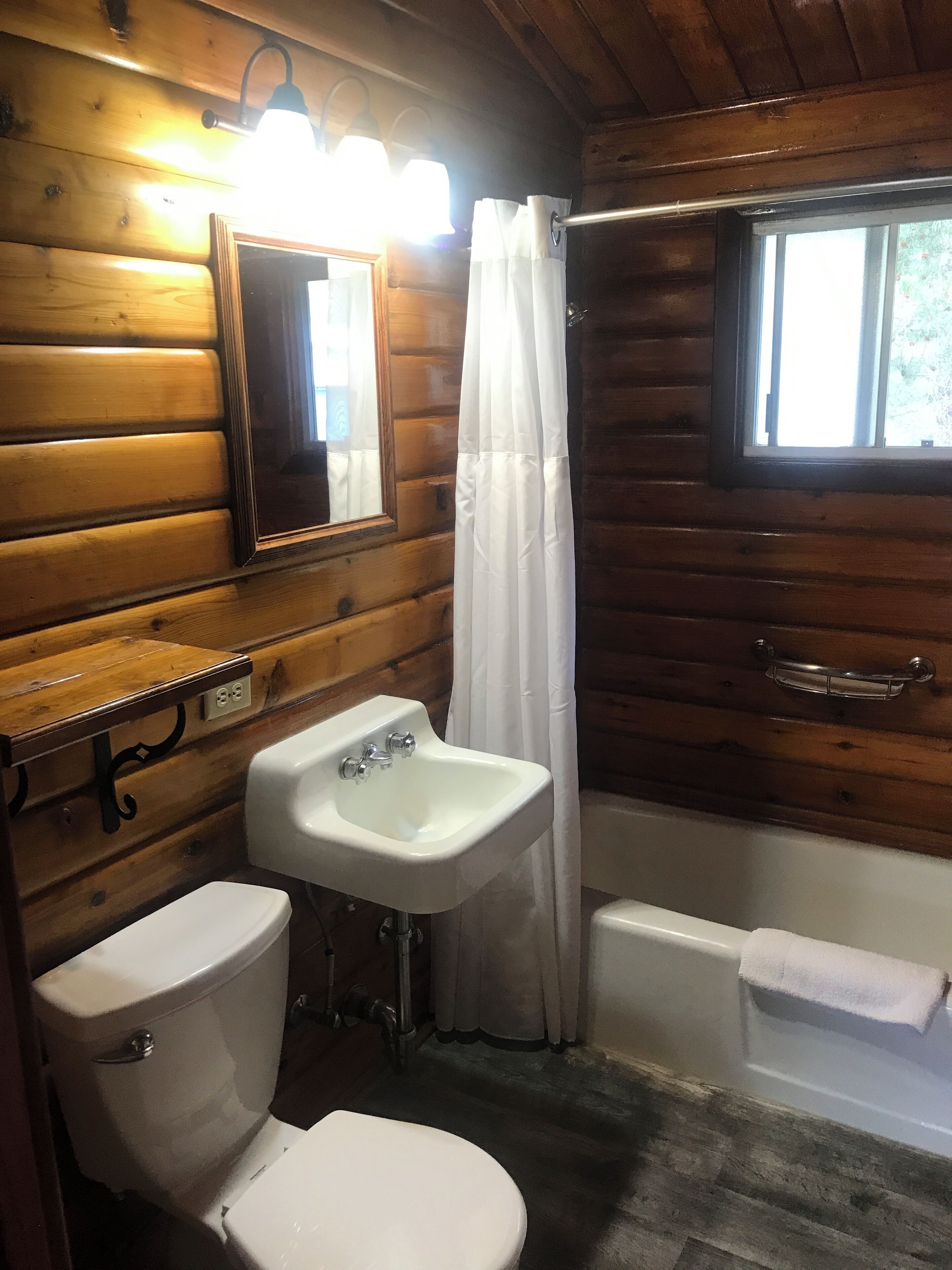 A wooden cabin bathroom with a toilet, sink, and bathtub.