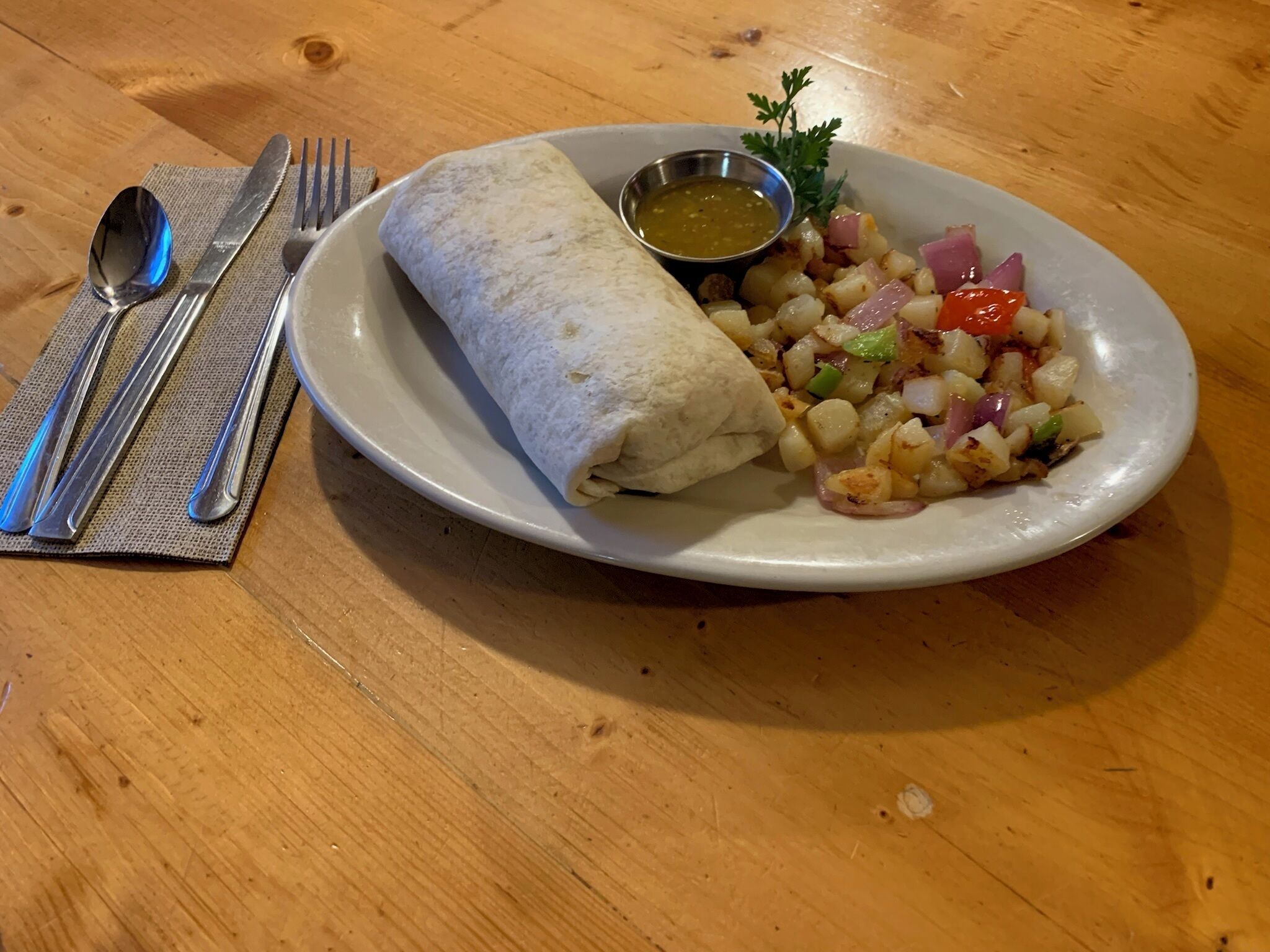 Ein Teller mit einem Burrito, einem kleinen Salat und einer Soße auf einem Holztisch.