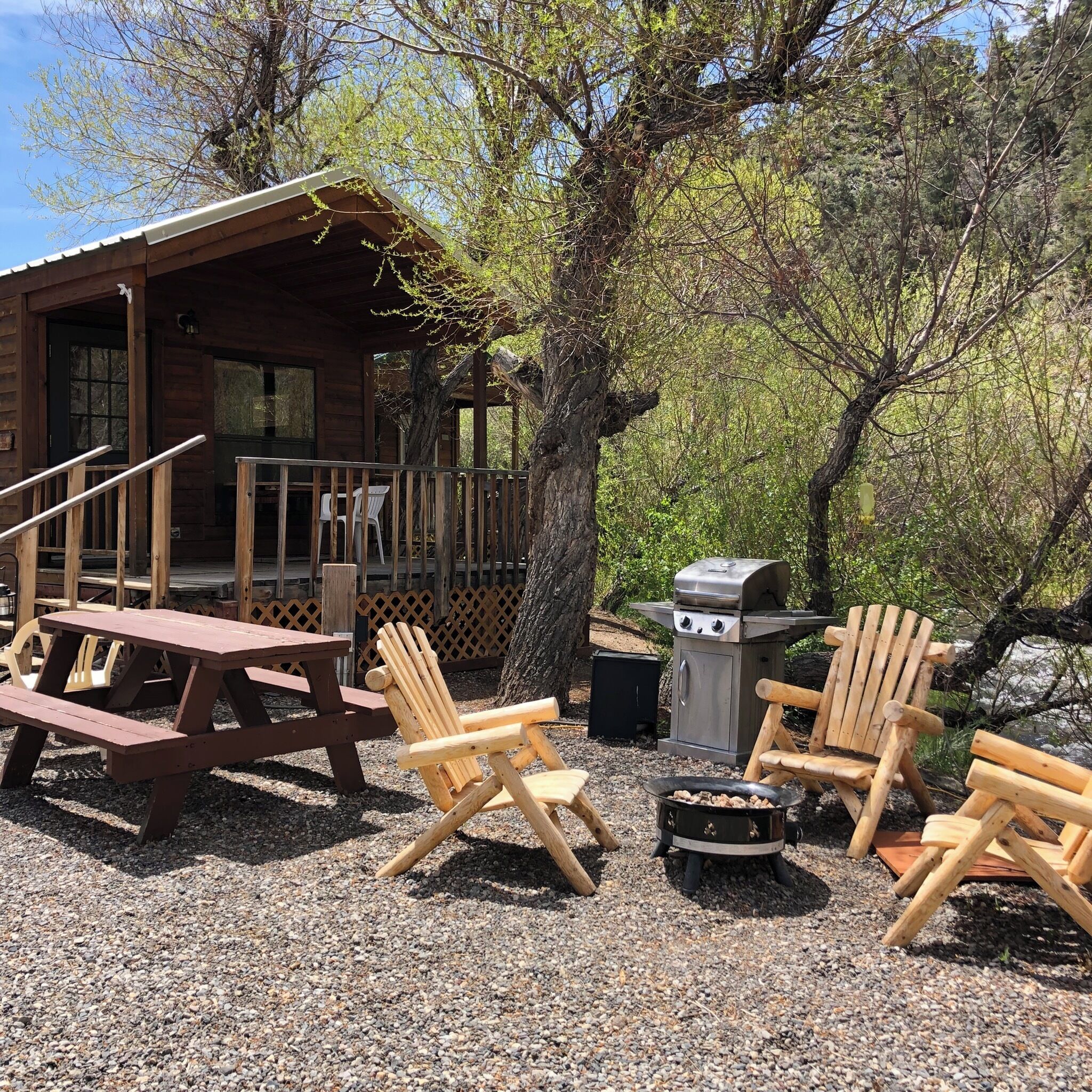 A rustic cabin with a wooden deck, picnic table, and Adirondack chairs.