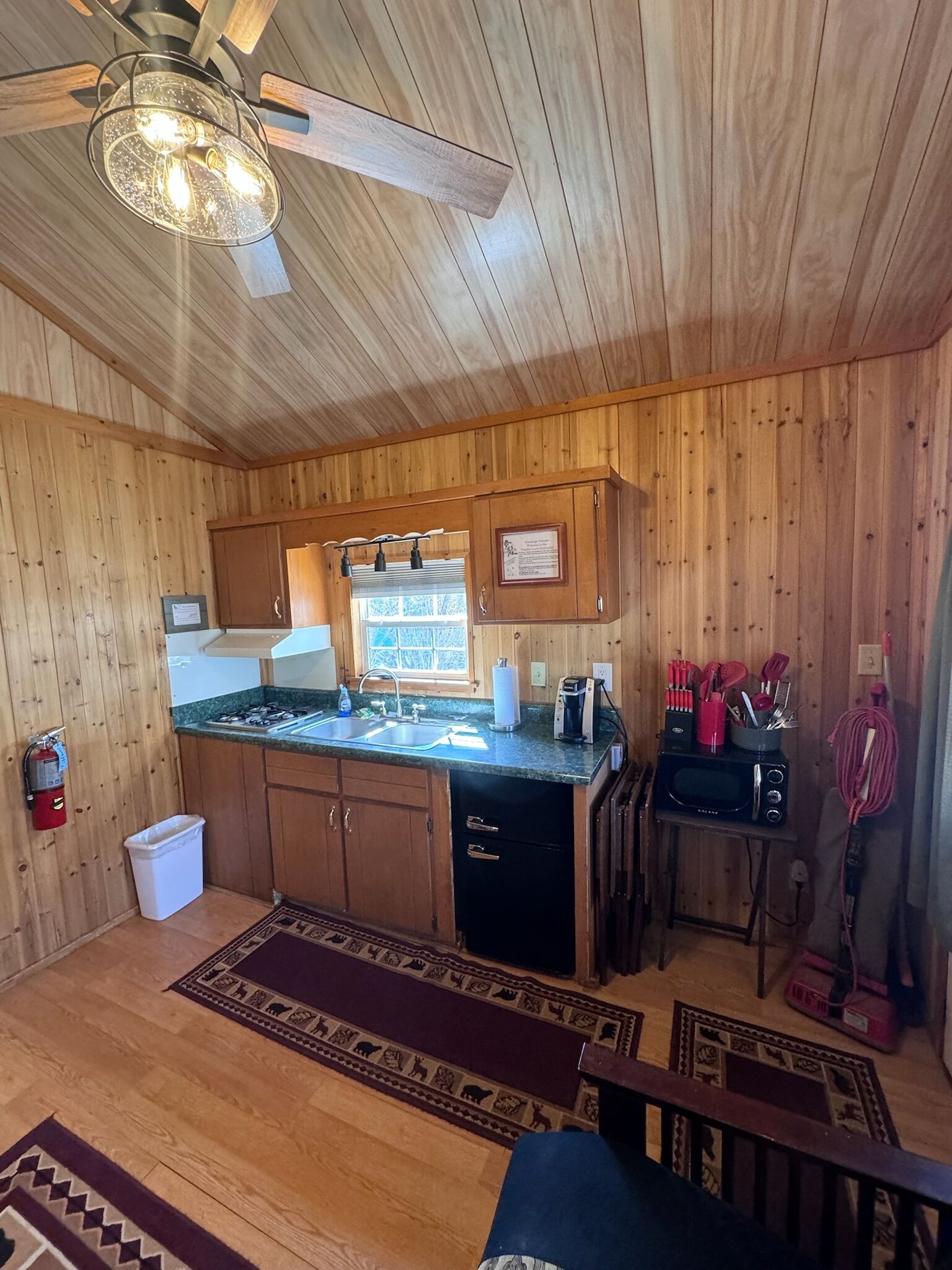 A wooden cabin kitchen with a gas stove, sink, and a ceiling fan.