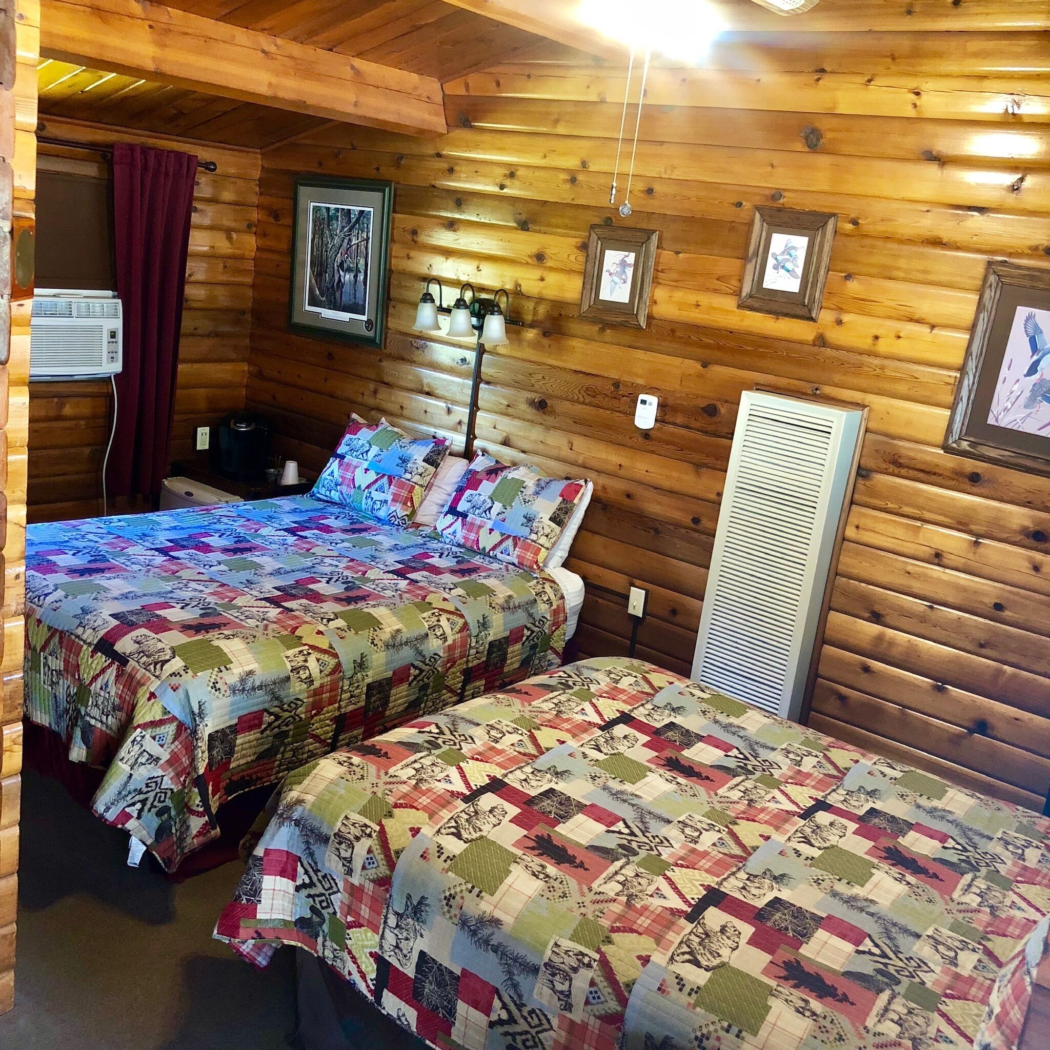 A cabin-style room with two beds, wooden walls, a ceiling fan, and a framed picture on the wall.