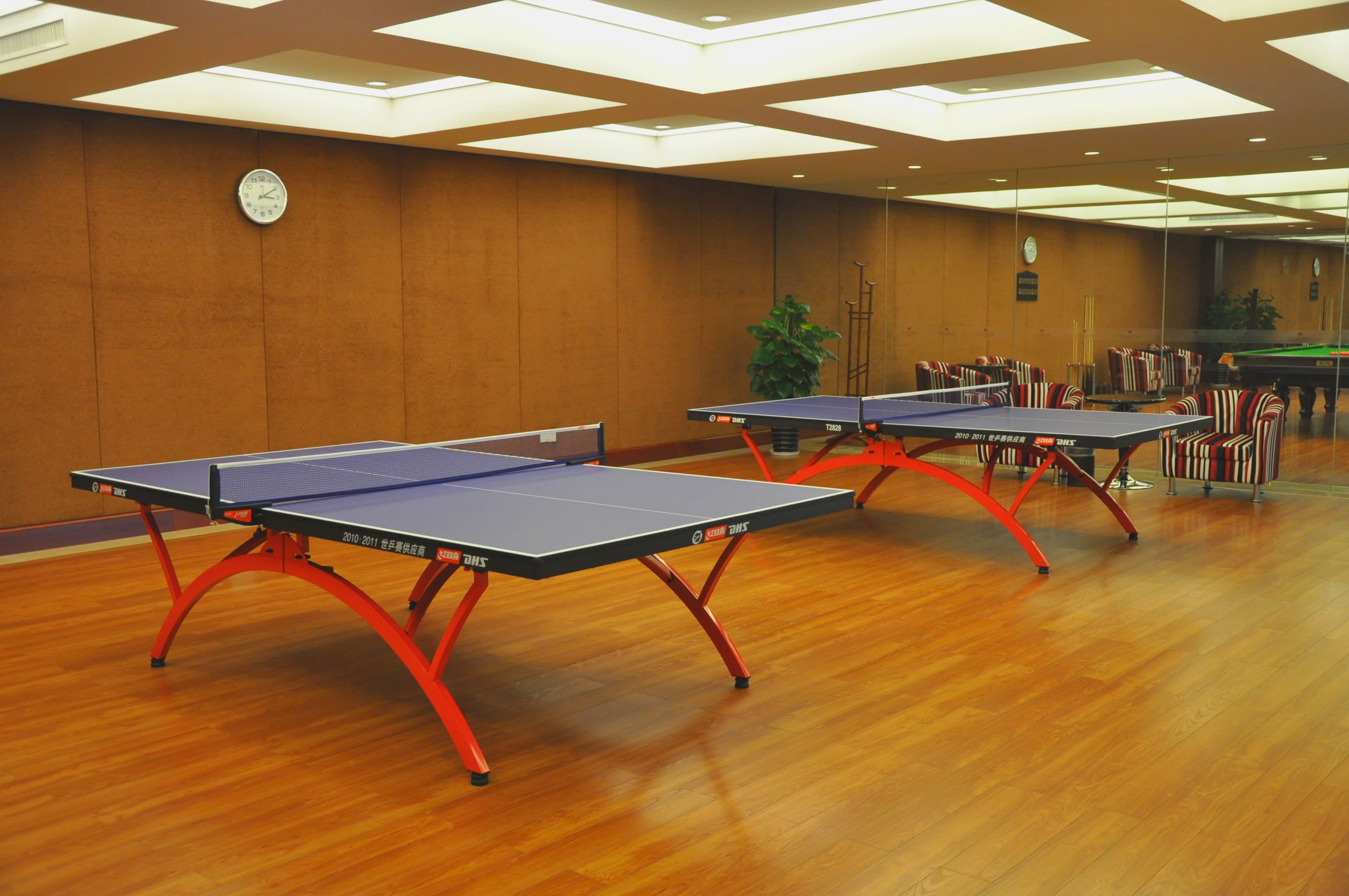 A room with two ping pong tables, wooden flooring, and a clock on the wall.