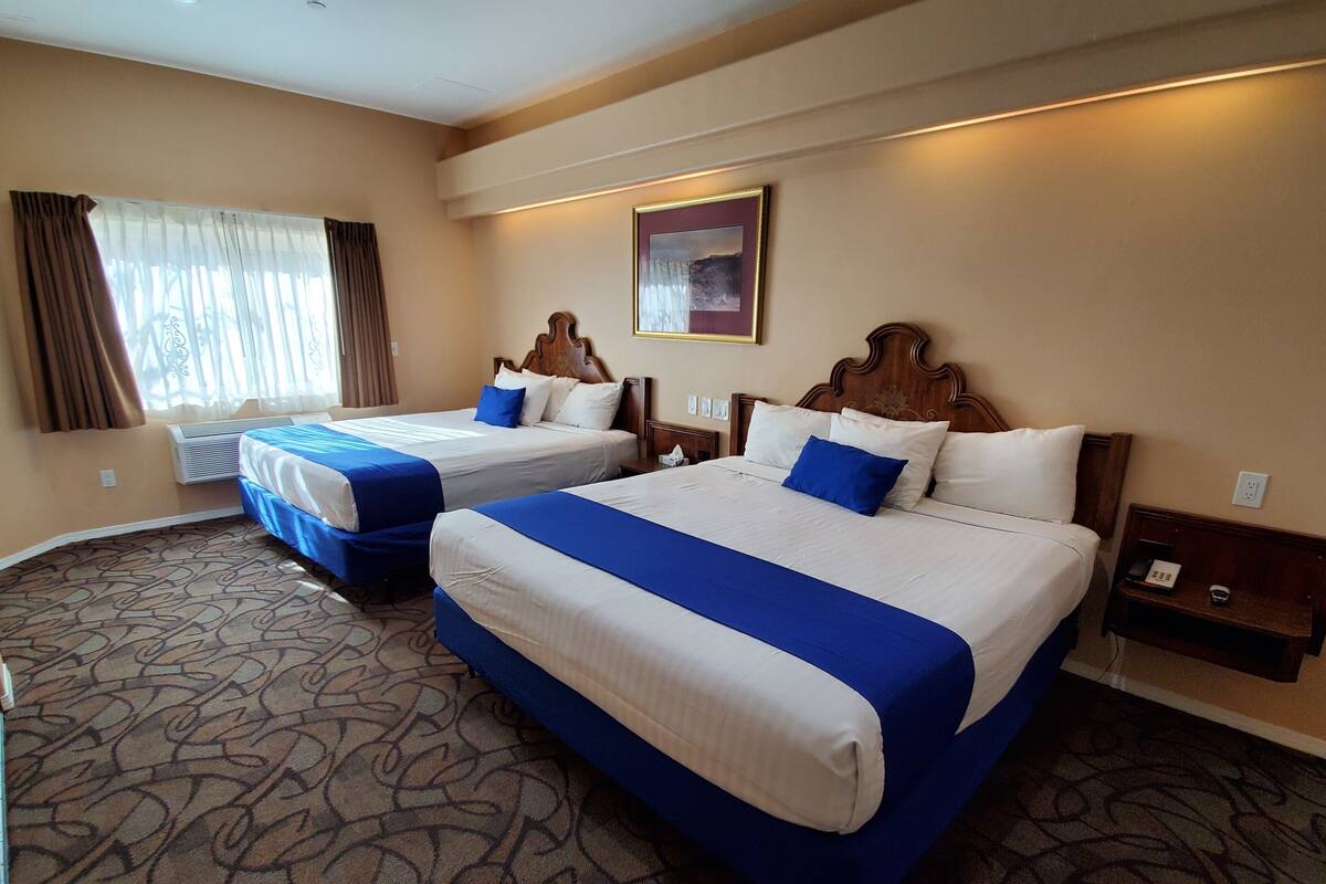 A hotel room with two beds, a patterned carpet, a window with curtains, and a painting on the wall.