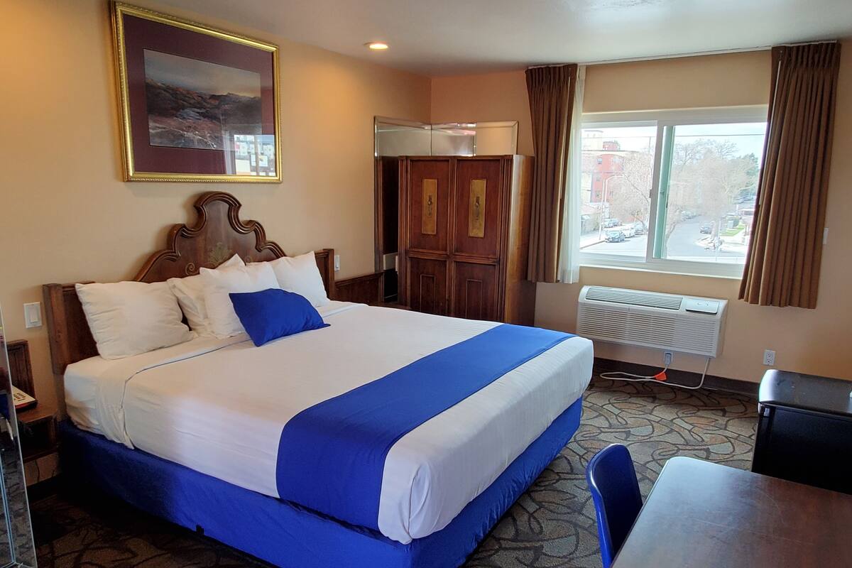A hotel room with a large bed, a desk, a wardrobe, and a window with curtains.