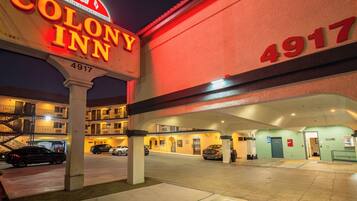 A hotel entrance with a neon sign, a visible address number, and a parking area.