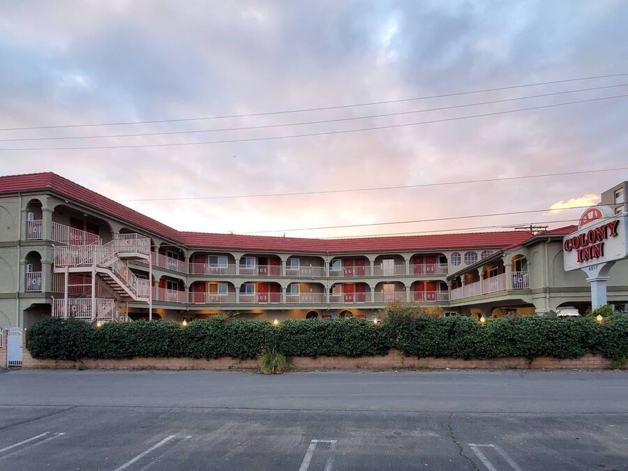 A multi-story motel with a red roof, balconies, and a parking lot in front.
