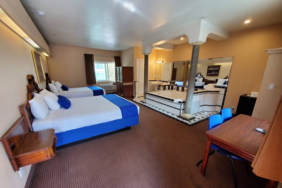 A hotel room with two beds, a large mirror, a bathtub, and a small table.