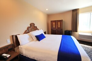 Habitación de hotel con una cama grande, cabecera de madera, escritorio con teléfono y armario.