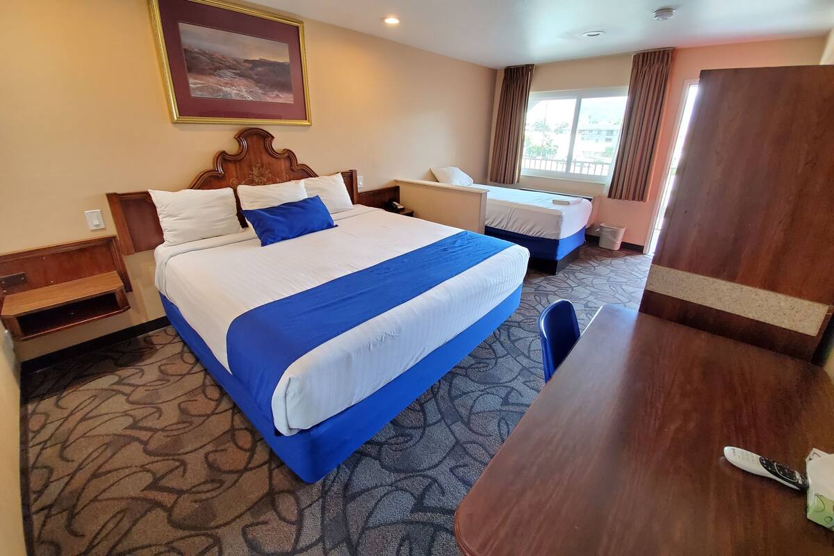 A hotel room with a large bed, a desk, a chair, a nightstand, and a window with curtains.