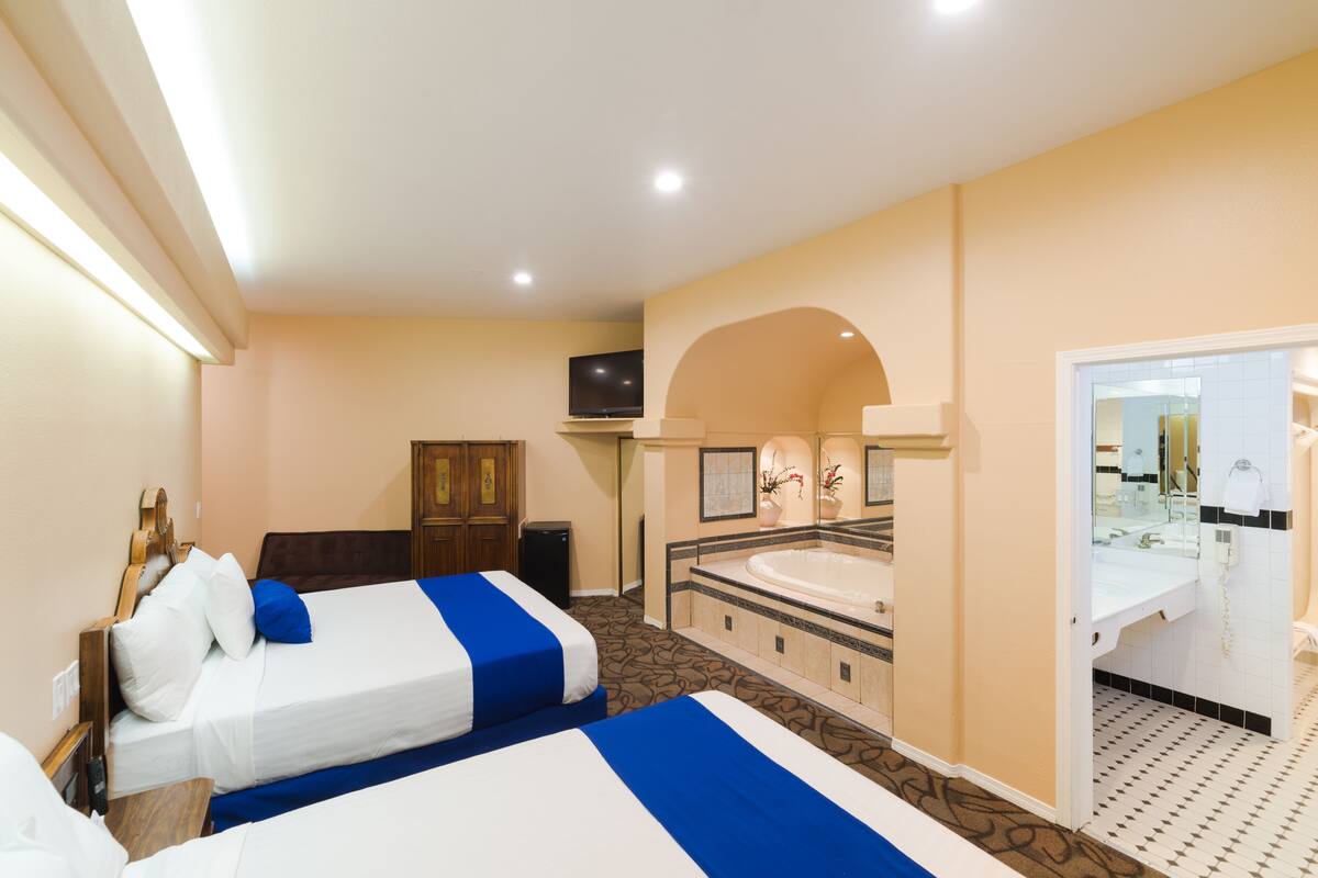 A hotel room with two beds, a bathroom with a bathtub, and a television.