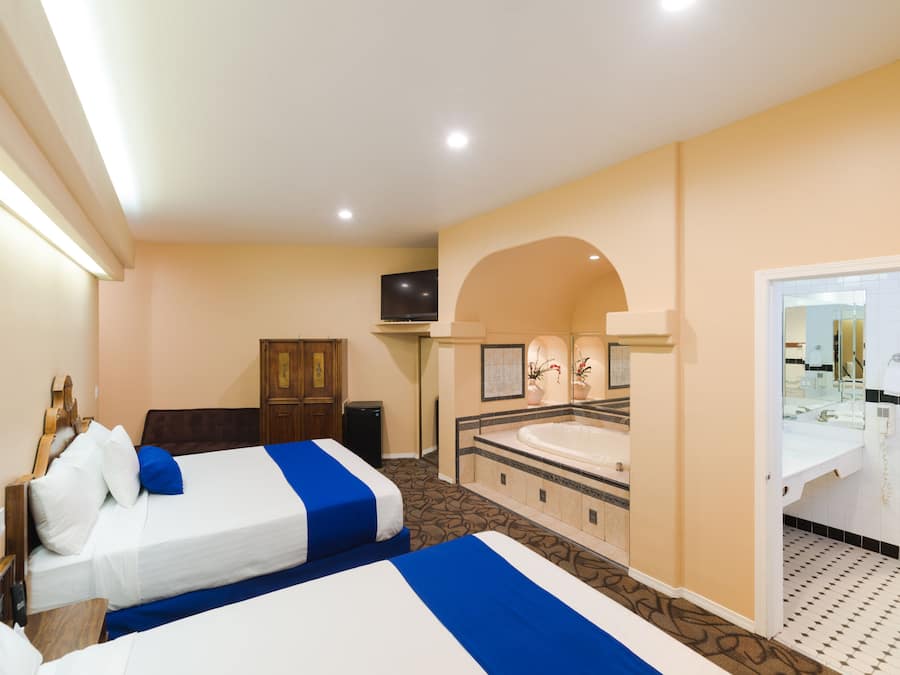 Quarto de hotel com duas camas, banheiro com banheira e televisão.