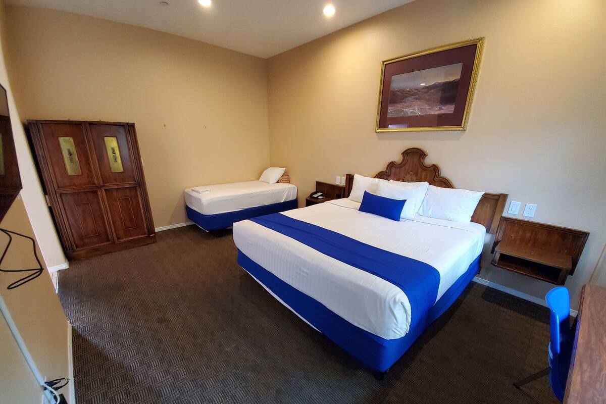 A hotel room with two beds, a wooden wardrobe, a framed picture on the wall, and a carpeted floor.