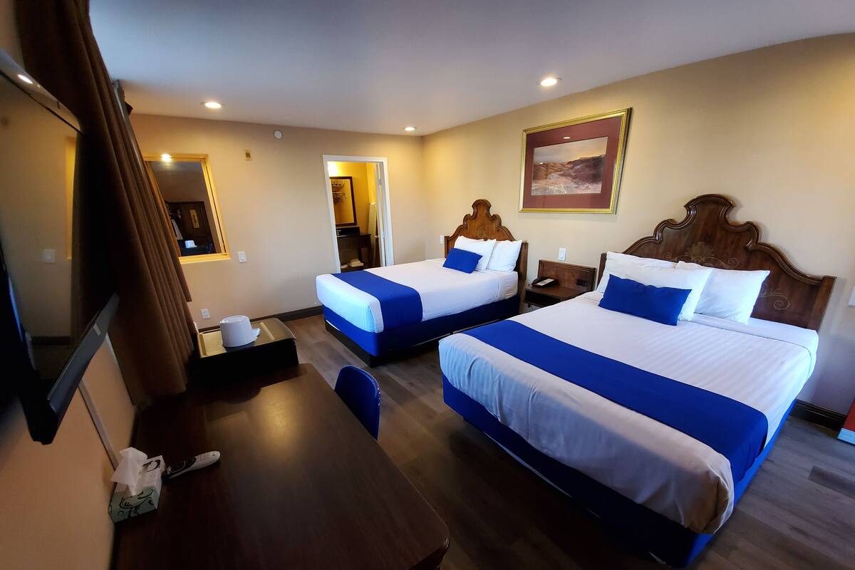 A hotel room with two beds, a desk, a chair, and a mirror.