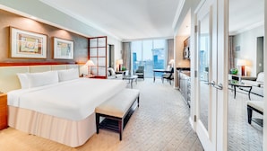 Quarto de hotel com uma cama grande, um banco, uma escrivaninha e vista para a cidade.