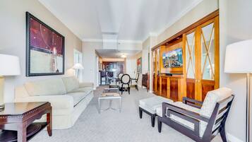 A spacious living room with a sofa, coffee table, and armchairs. A dining area with chairs and a table is visible in the background.