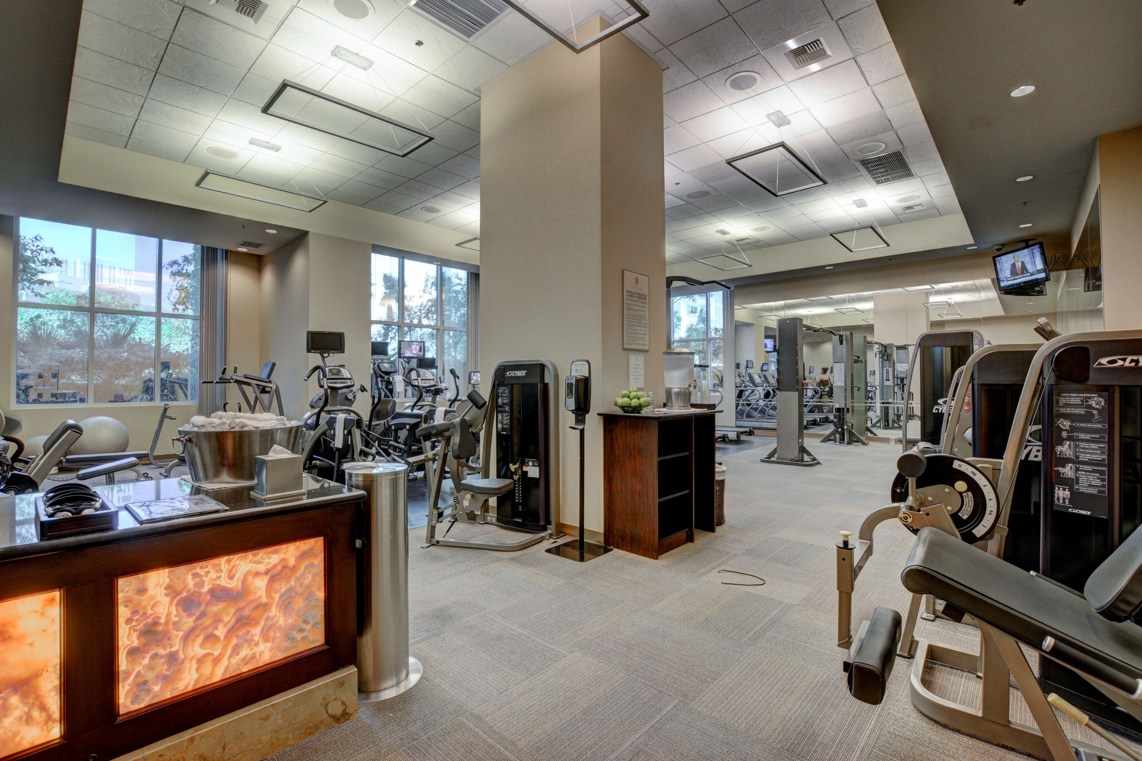 Un gimnasio moderno con diversos equipos de ejercicio, un mostrador de recepción y amplias ventanas que ofrecen luz natural.