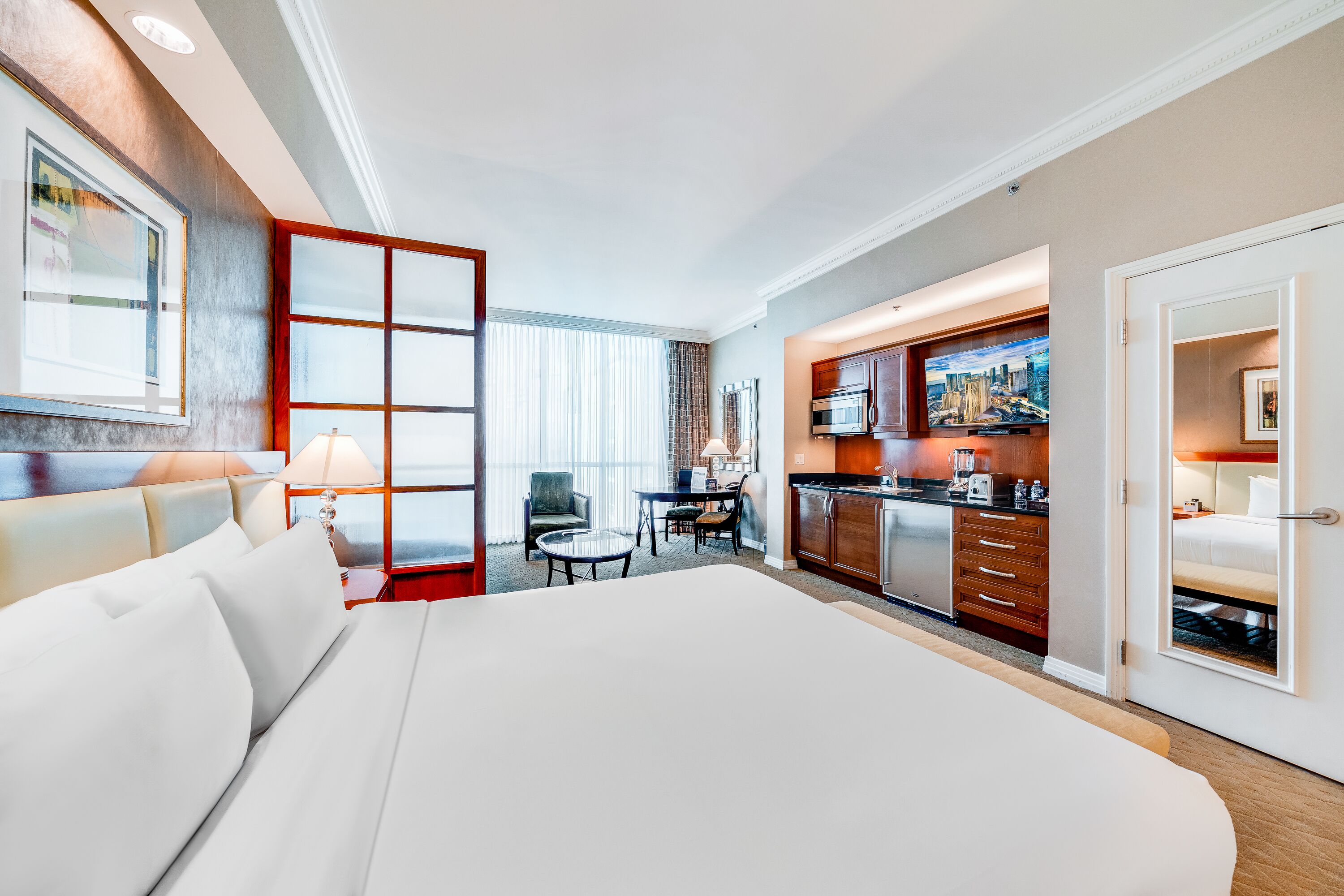 A hotel room with a large bed, a dining area, and a kitchenette.