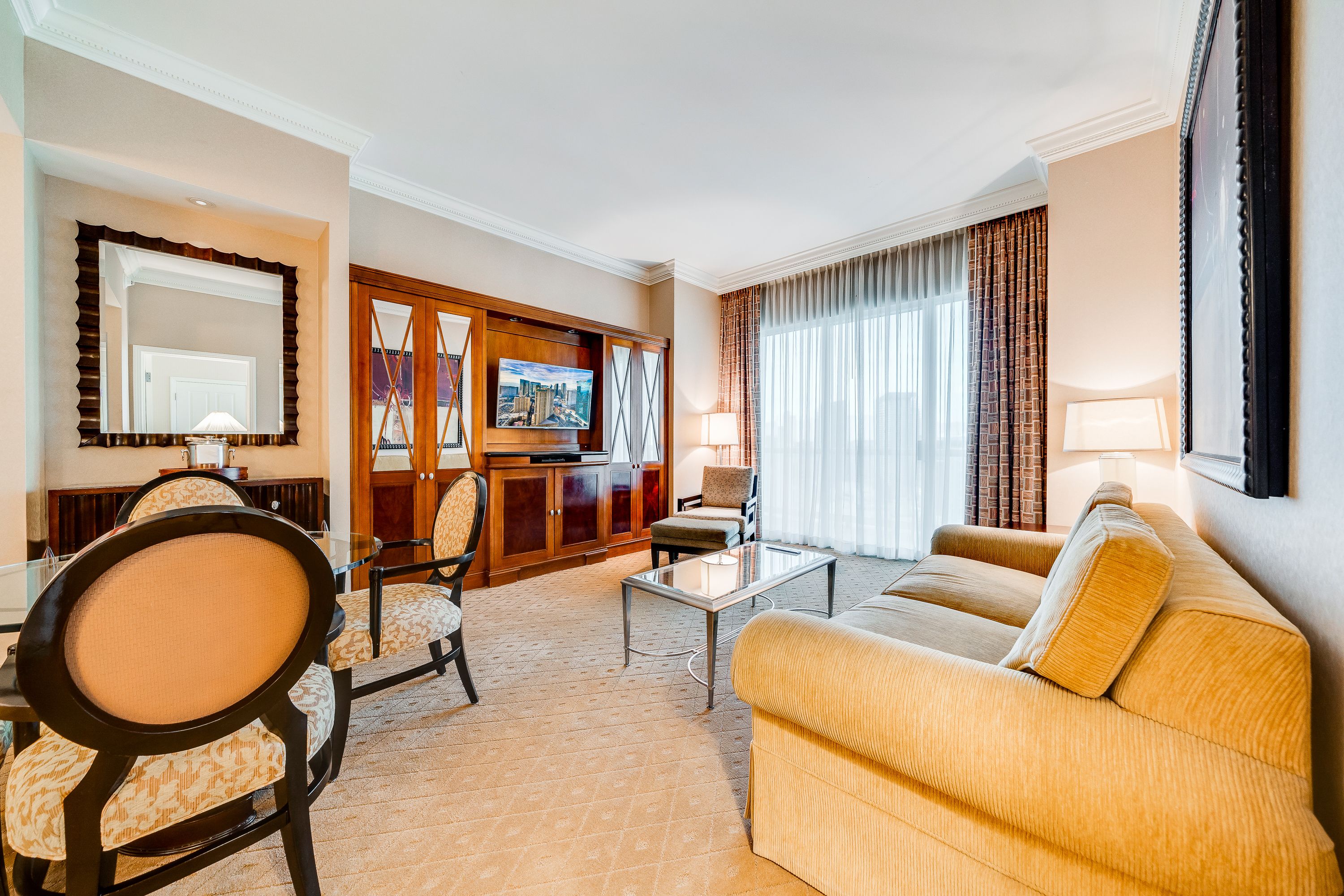A hotel room with a sofa, armchair, dining table, and a TV.