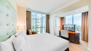 A hotel room with a large bed, a television, a desk, and a view of the city.