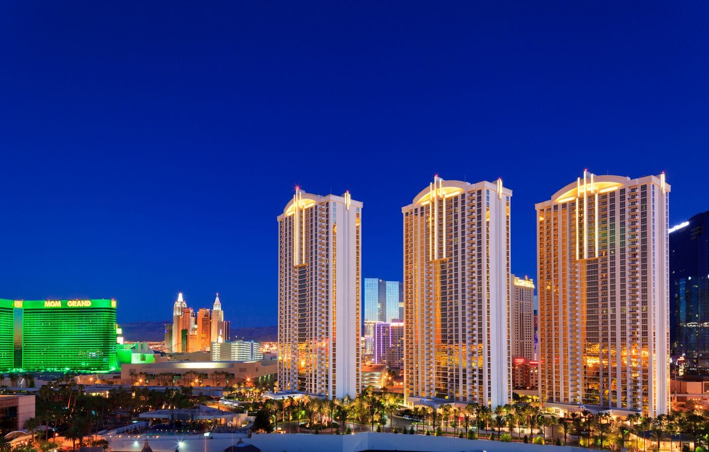 Un hotel di grandi dimensioni con numerosi piani, un casinò ben visibile sullo sfondo e un moderno skyline urbano illuminato.