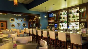 Zona de bar con varias opciones de asientos, una amplia variedad de licores y espejos decorativos en la pared.