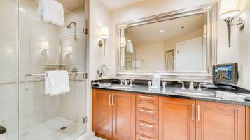 A modern bathroom with a glass shower, wooden cabinets, a large mirror, and a flat-screen TV.