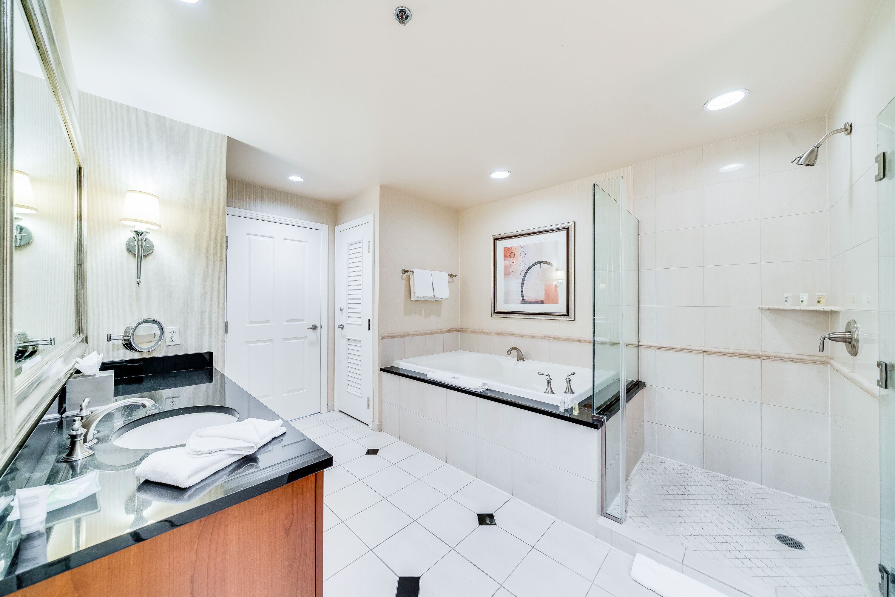 Een moderne badkamer met een dubbele wastafel, een grote spiegel, een douche met glazen wanden en een ingelijst kunstwerk aan de muur.