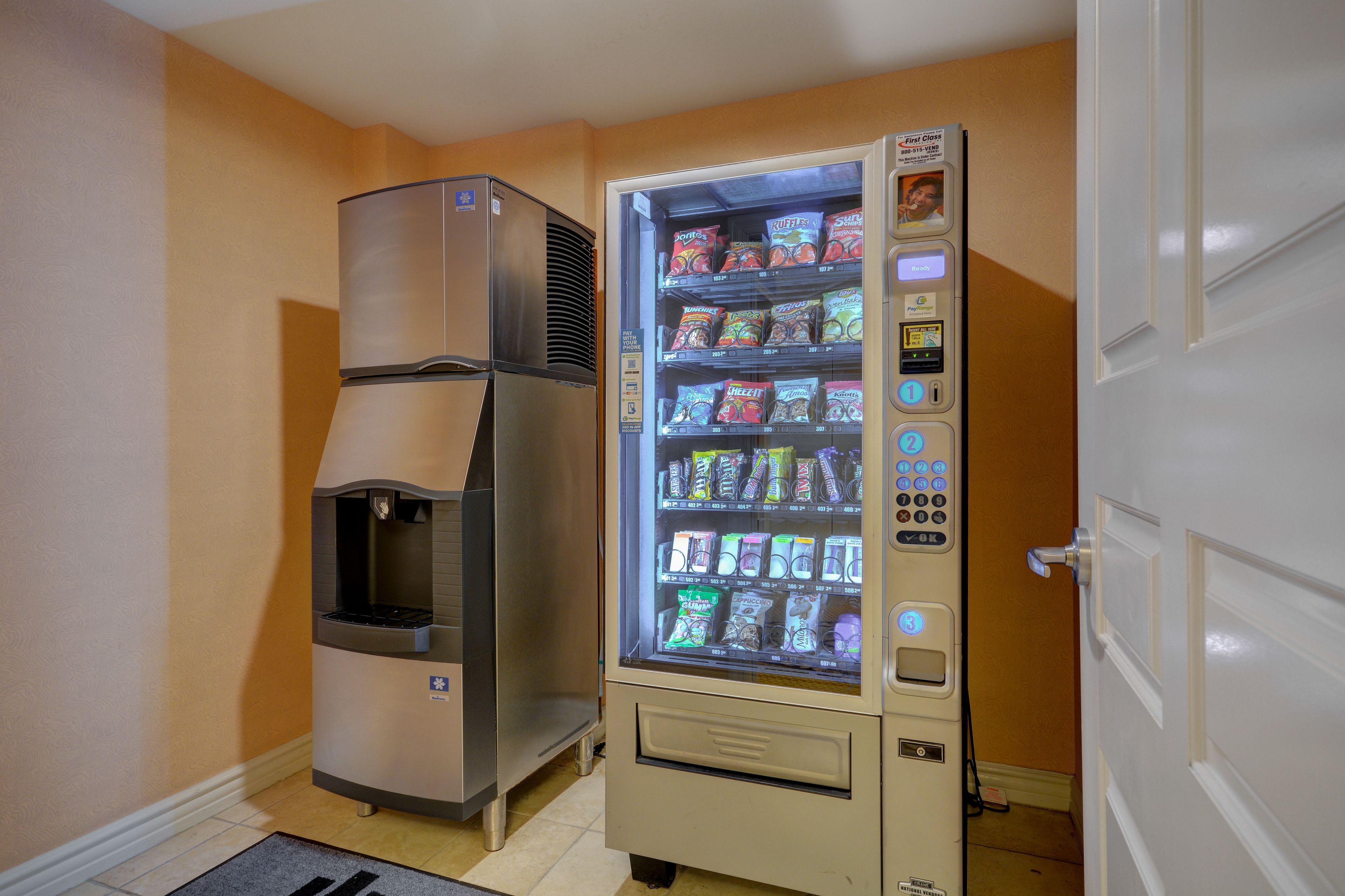 Een automaat met snacks en een drankdispenser in een kamer met oranje muren en een witte deur.