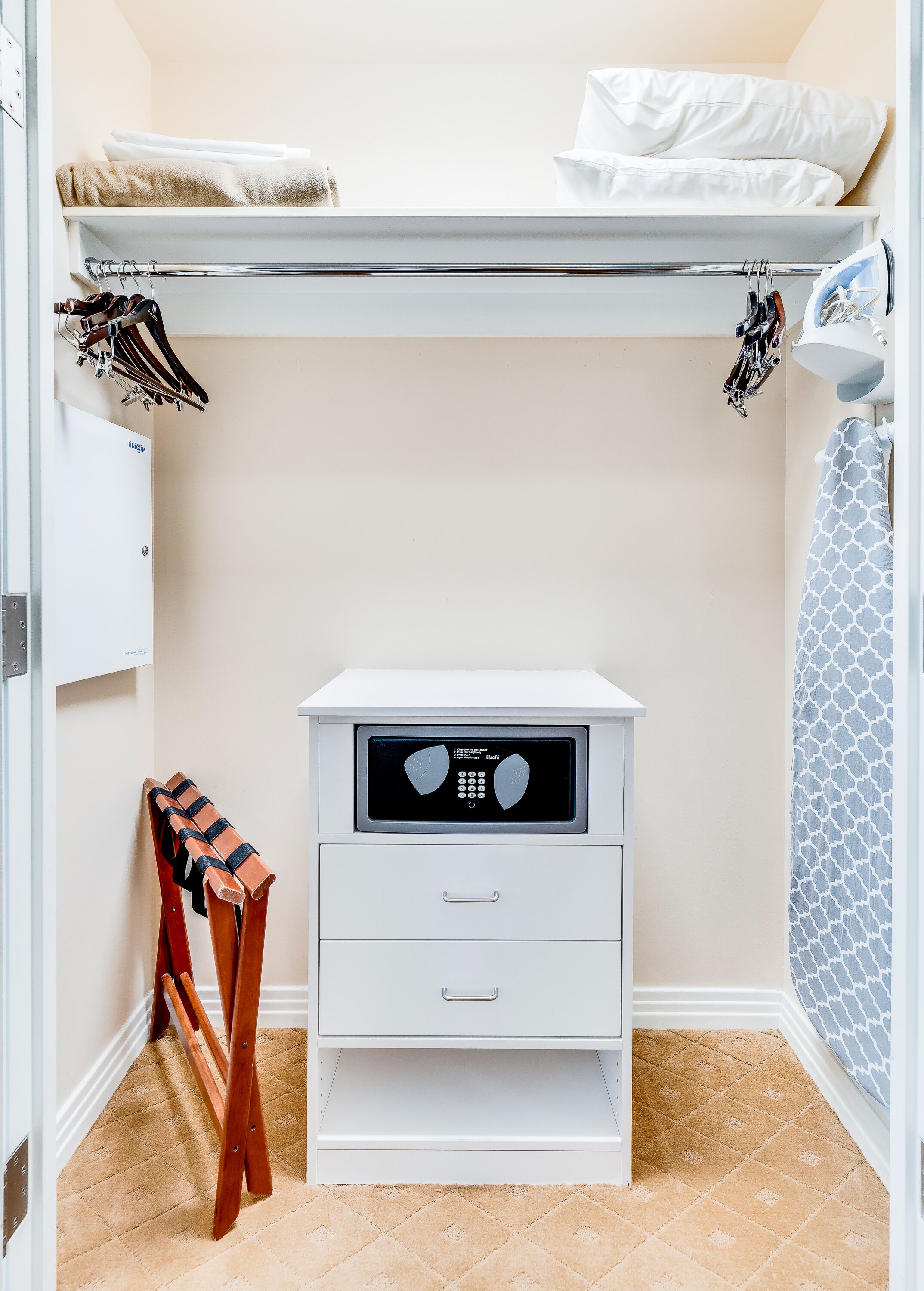 A small, white, walk-in closet with a built-in dryer, a wooden shoe rack, and a patterned shower curtain.