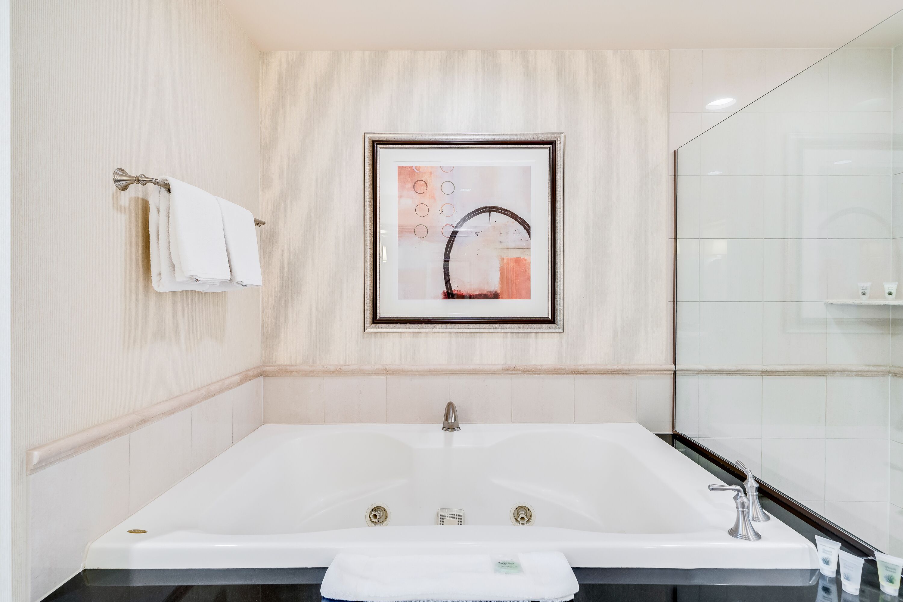 A modern bathroom with a large bathtub, a framed artwork above the sink, and a glass shower enclosure.