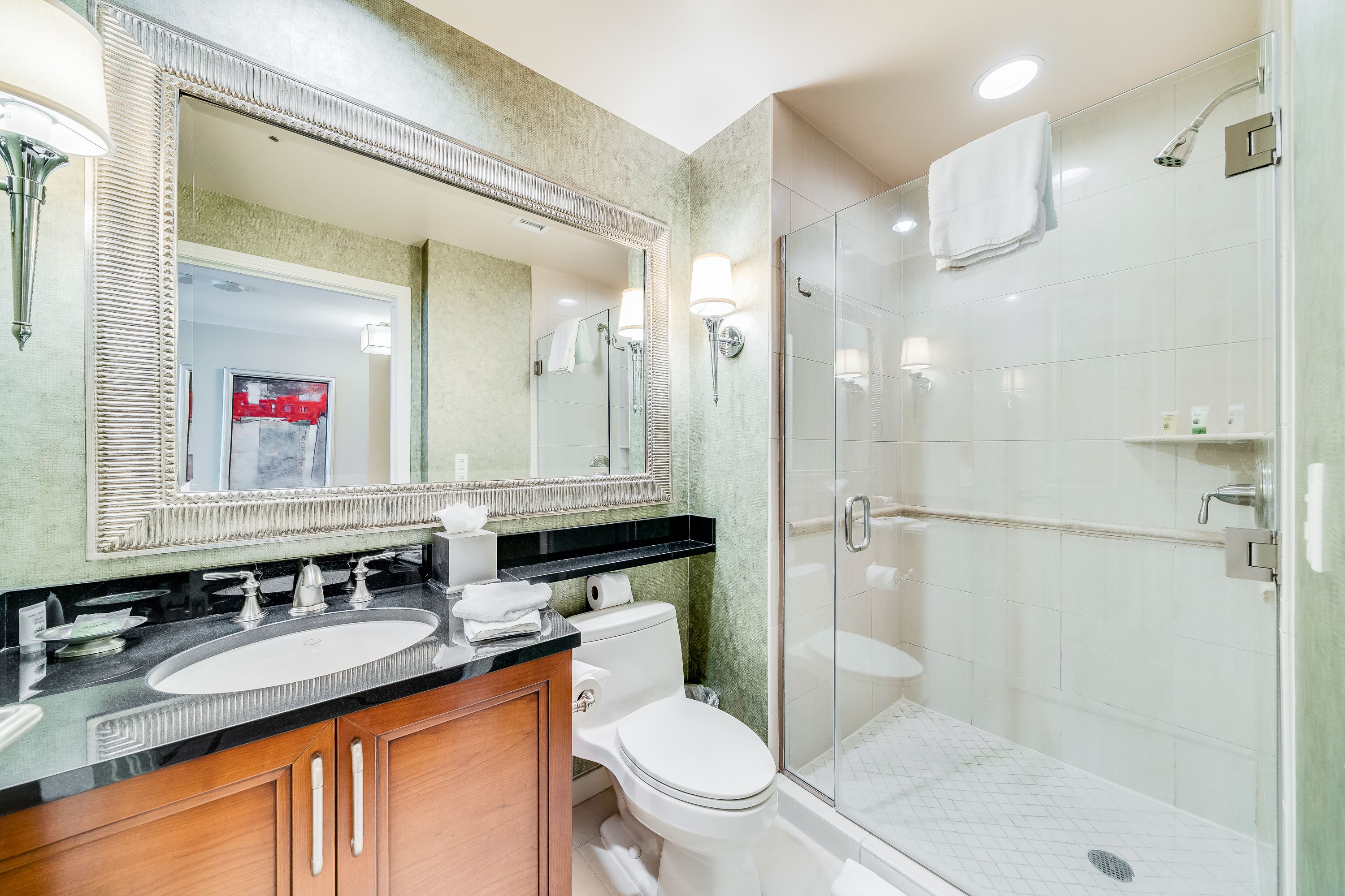 A modern bathroom with a large mirror, two sinks, a toilet, and a glass-enclosed shower.