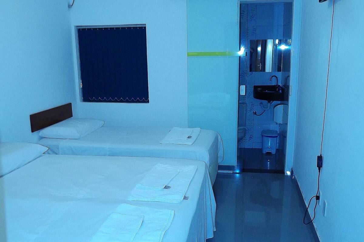 Ein Hotelzimmer mit zwei Einzelbetten, einem Fenster, einem Waschbecken und einem Fernseher.